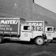 Two Oscar Mayer delivery trucks wait at a loading dock, Madison, Wisconsin in 1930. One of the trucks has a sign for ‘Bacon’ on the side, the other ‘German Wieners.’